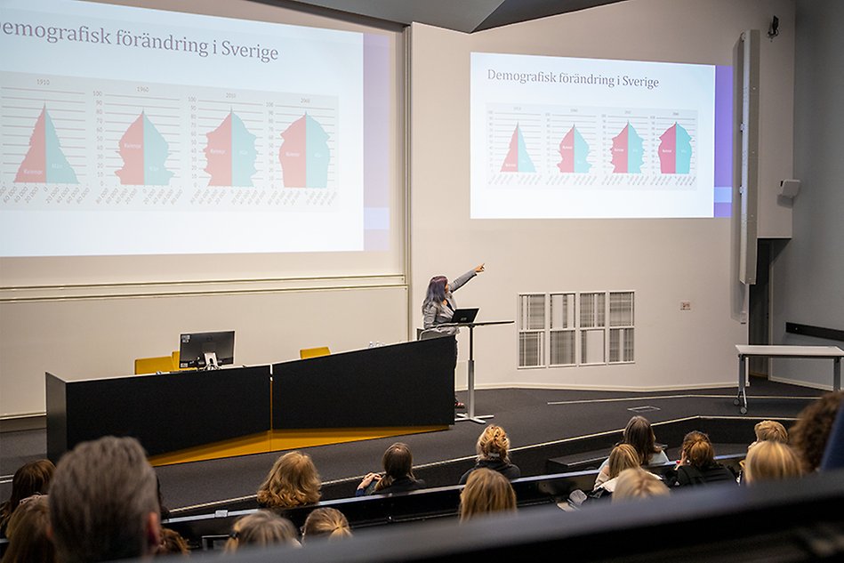 Kvinna håller i en föreläsning och pekar på presentationen bakom henne