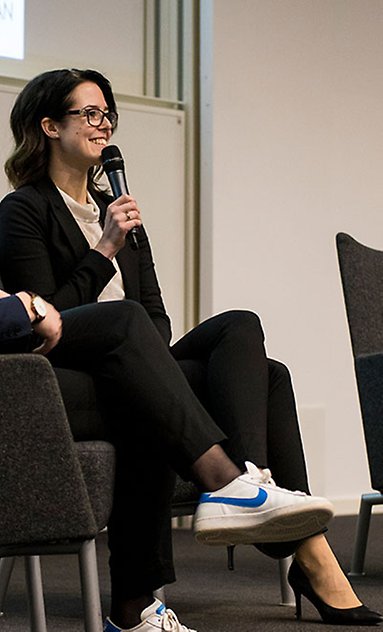 En kvinna sitter i en fåtölj på scenen. Hon håller i en mikrofon och svarar på frågor från publiken.