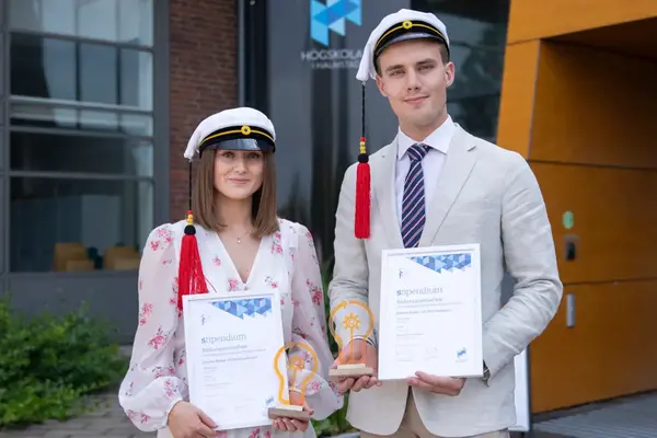 Två finklädda studenter ler mot kameran. Båda håller i ett varsitt diplom och statyett. Foto.