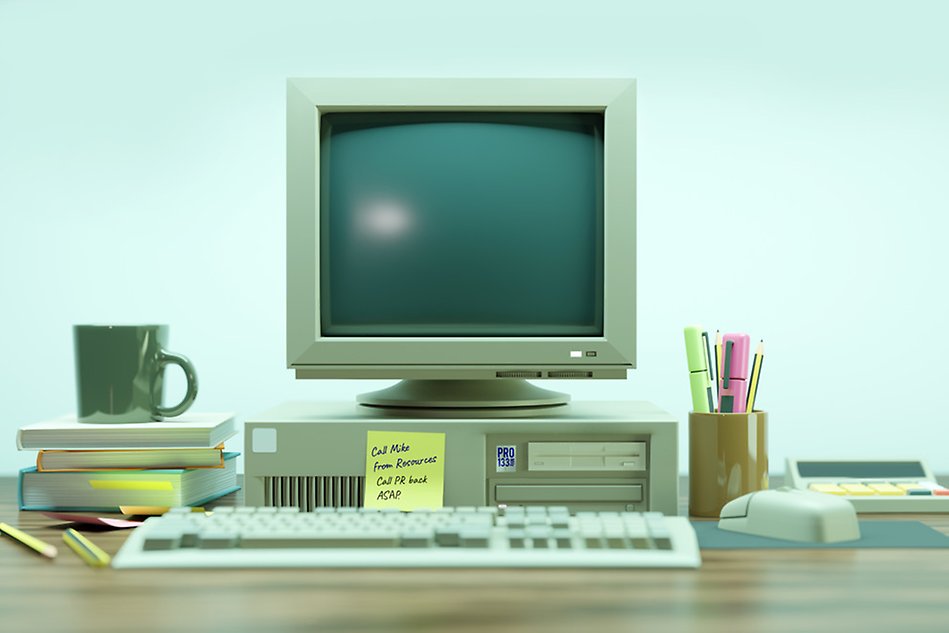 An older looking computer on a desk filled with post its, pens, staplers and other office materials. Photo.