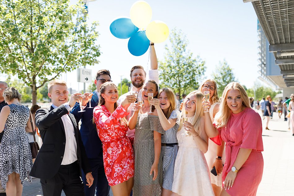 En grupp glada studenter står utanför Halmstad Arena med ballonger och bubbelglas.