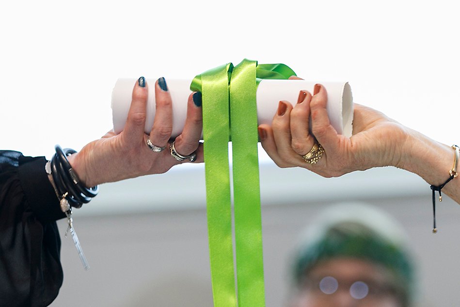 Diploma with a green ribbon being passed from one hand to another. Photo.