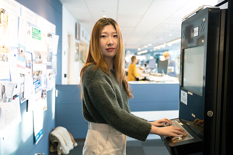 En kvinnlig student står vid en servicestation i Servicecenter och tittar in i kameran. Foto.