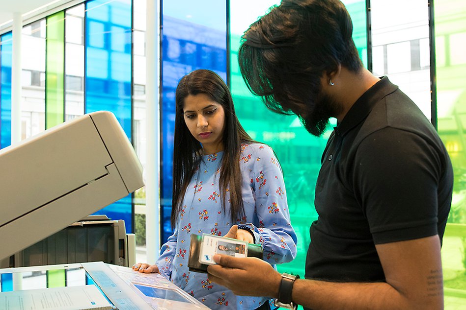 A woman and a man stand at a printer. Photo. 