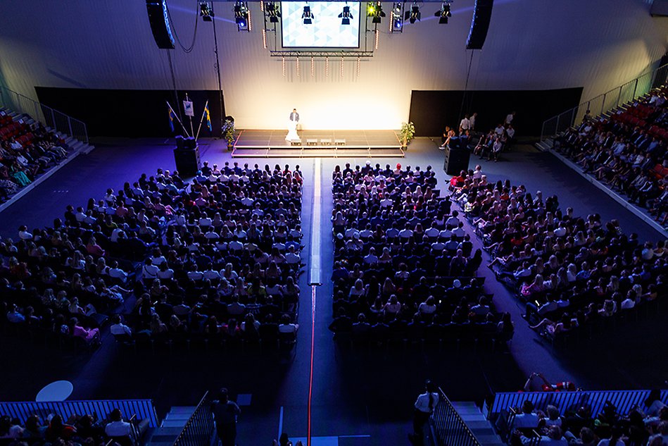 Person on stage in front of arena full of spectators. Photo. 