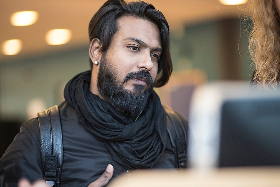 A man with black clothes and a beard is looking down at something. Photo. 