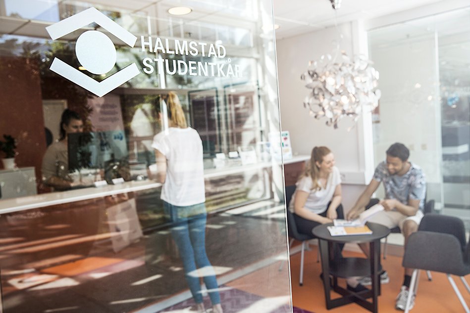 Glasvägg med texten Halmstad Studentkår, en reception syns bakom glaset. Foto.