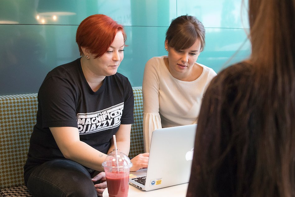 Two people are sitting on a couch looking down at a computer screen. Photo. 