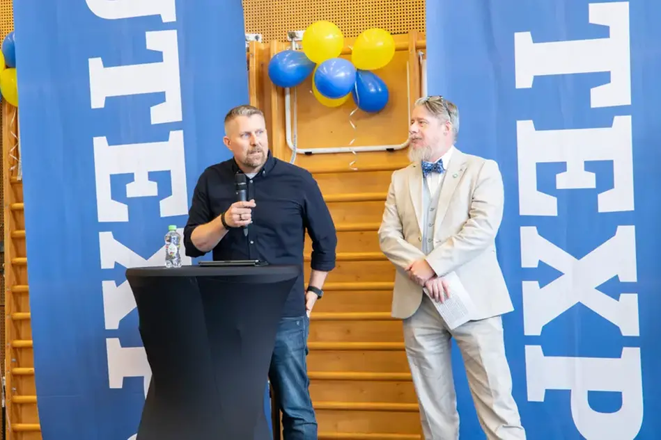 Två finklädda personer står vid ett podium. En håller tal.