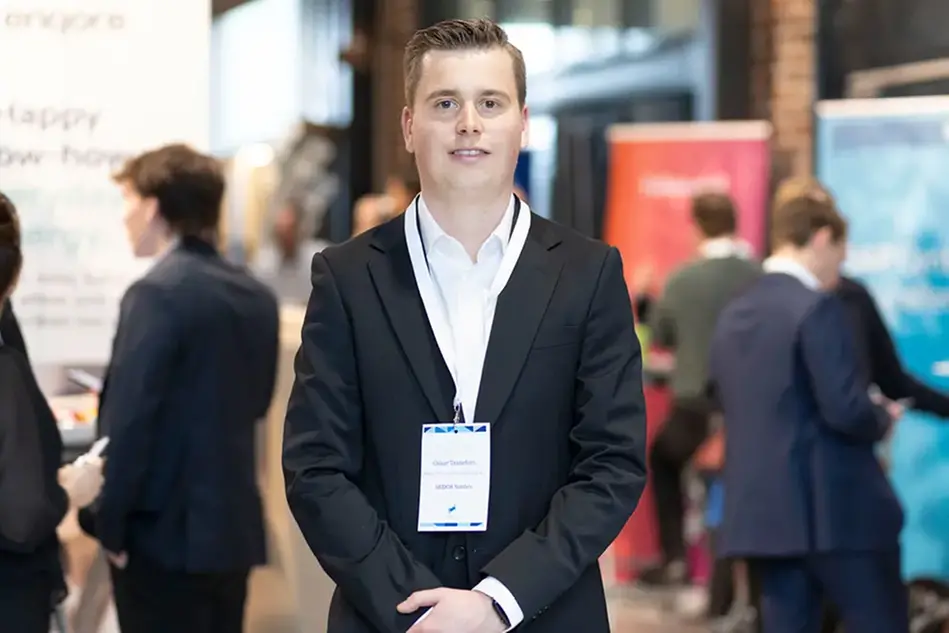 Person i kostym står i ett öppet utrymme fylld med montrar och människor.