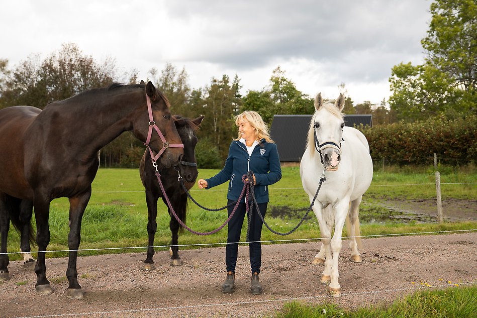 A person standing in the middle of three horses smiling. Photo.