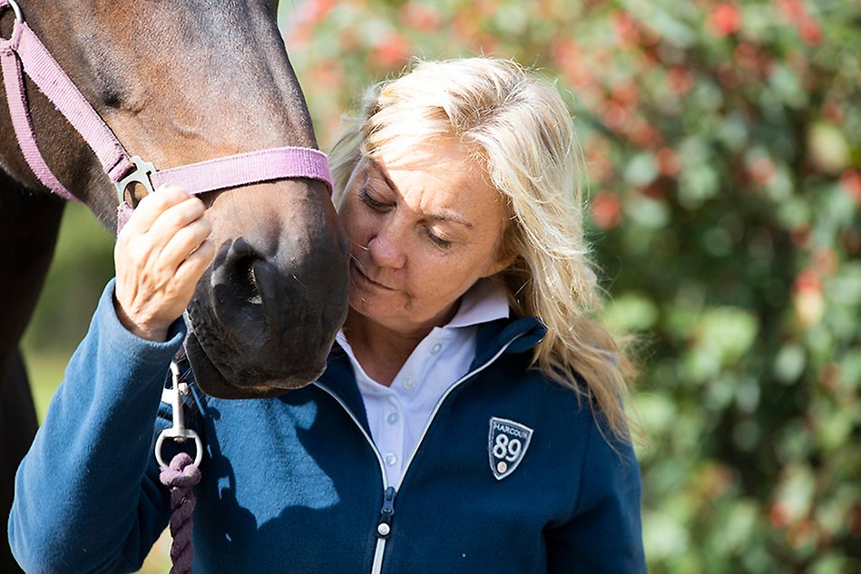 A person with blonde hair leaning in towards the muzzle of horse. Photo.