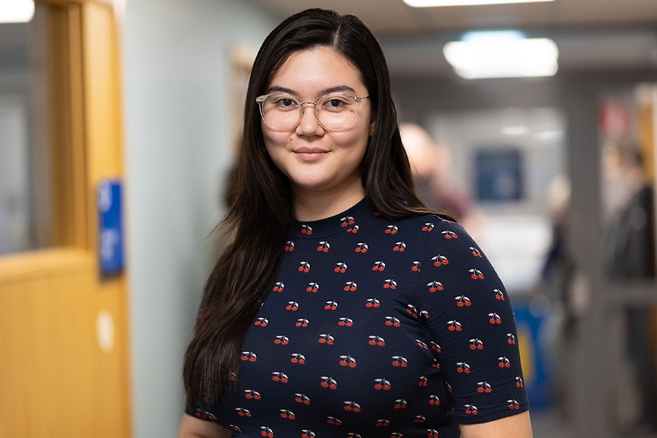 A woman with glasses looking into the camera. The background is blurred.