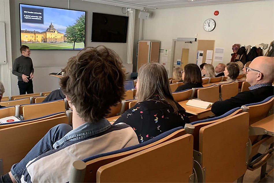 Personer sitter i en föreläsningssal och lyssnar till en talare.