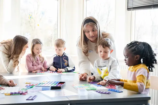 Två vuxna leker pedagogiskt med fyra barn i förskoleåldern.