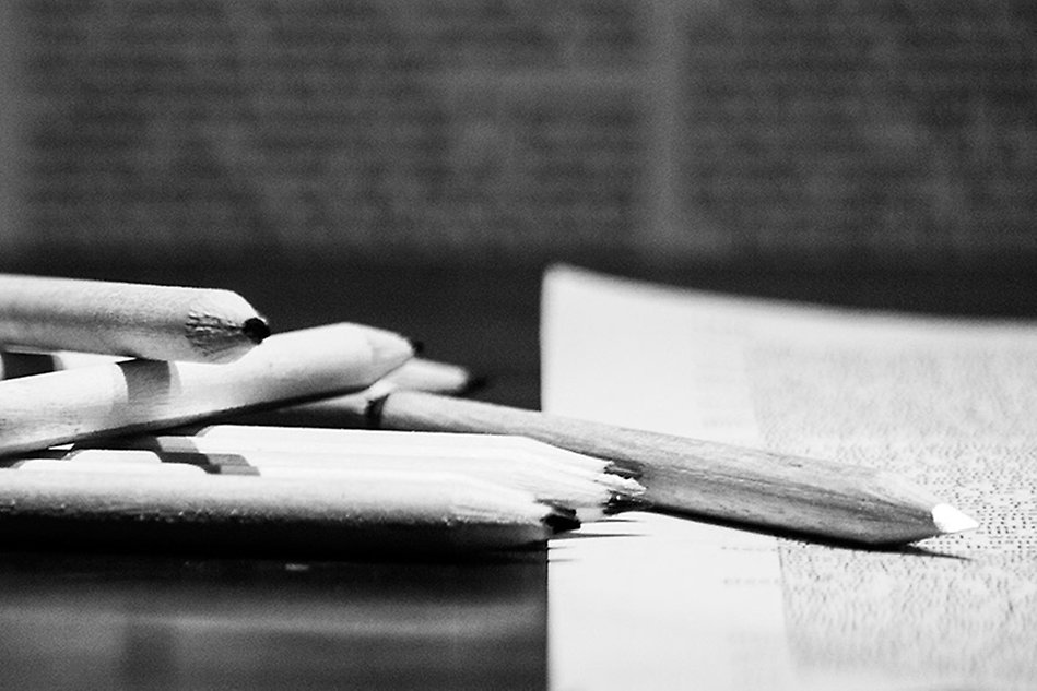 Black and white photo of some pencils lying on a book.