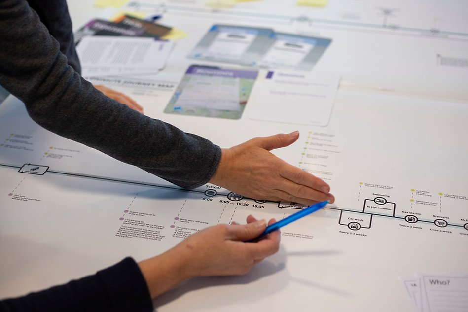 Hands from two different people gesturing over schematics on a table.