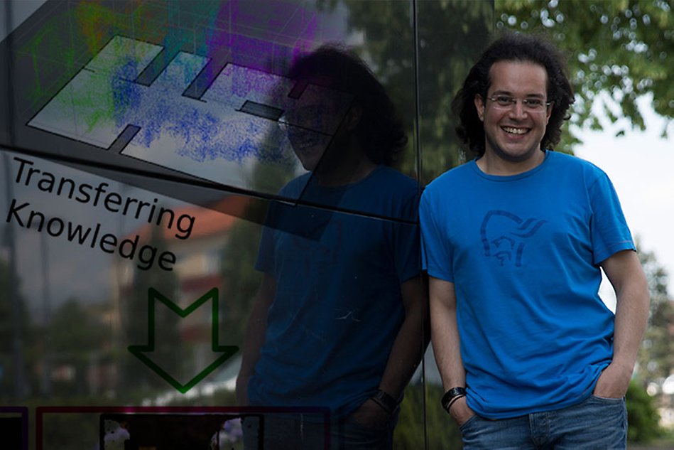 A man with dark hair wearing a bright blue T shirt is leaning against a black wall. A floor plan and the words Transferring Knowledge are superimposed on the wall.