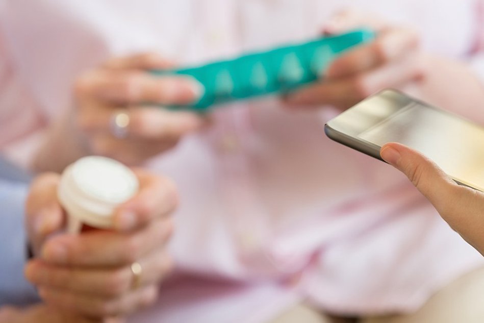 Closeup of elderly hands holding pill boxes and another hand holding a padlet.