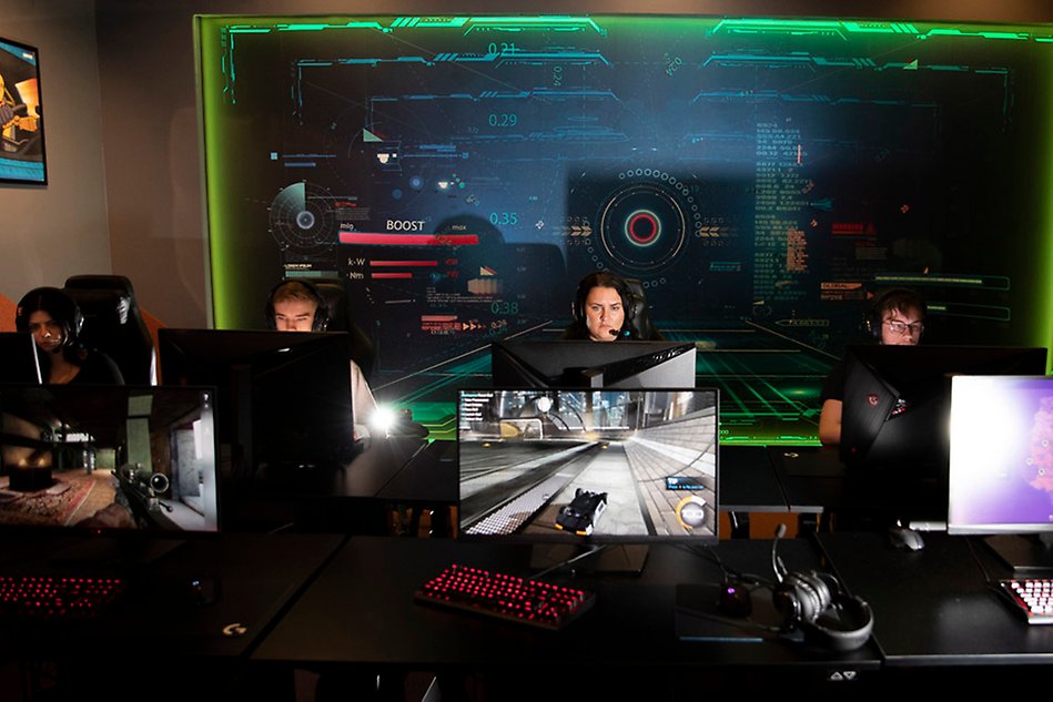fyra studenter sitter på rad och spelar dator i en mörk miljö
