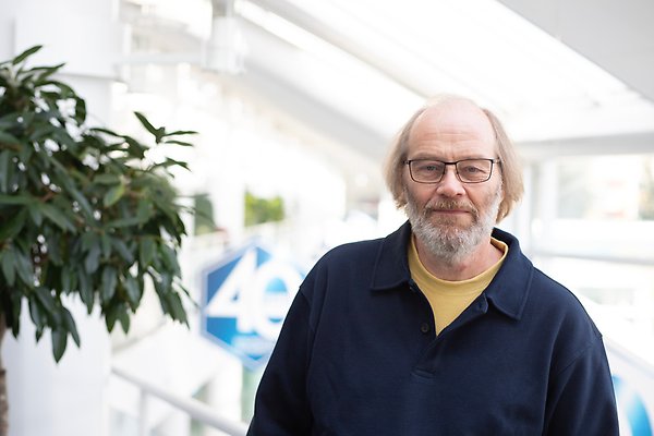 Porträtt av man med glasögon och skägg iklädd en blå tröja. Foto