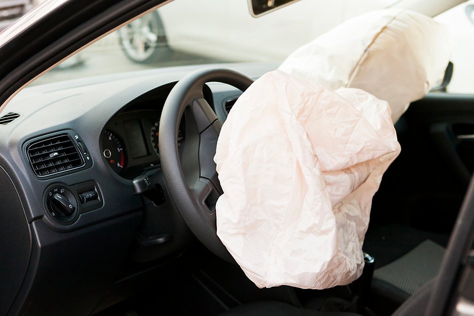 The dashboard of a car with a deployed airbag hanging from the steering wheel