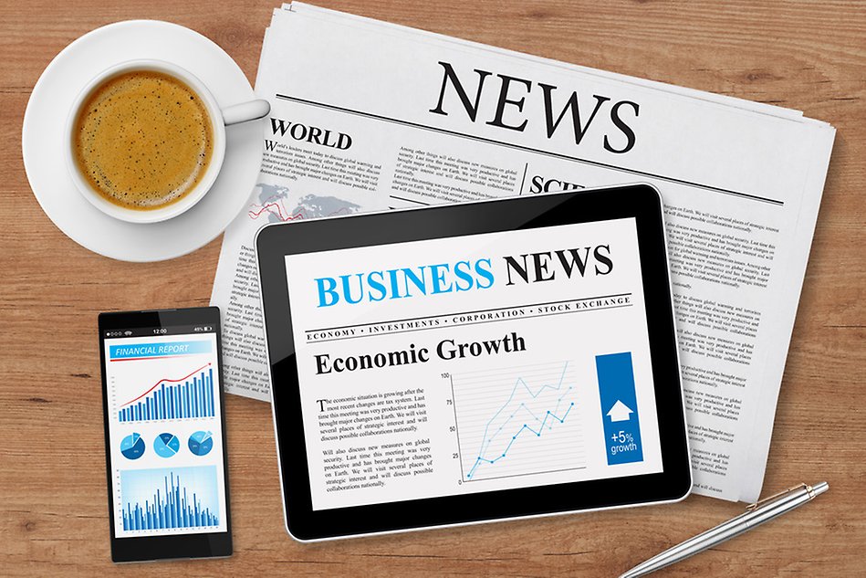 Kitchen table with a newspaper, tablet and mobile phone displaying news sites and coffee cup on it