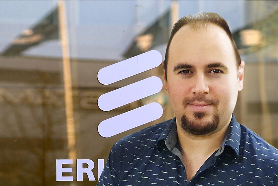 A portrait of a man standing in front of a window with the Ericsson logotype. Photo.