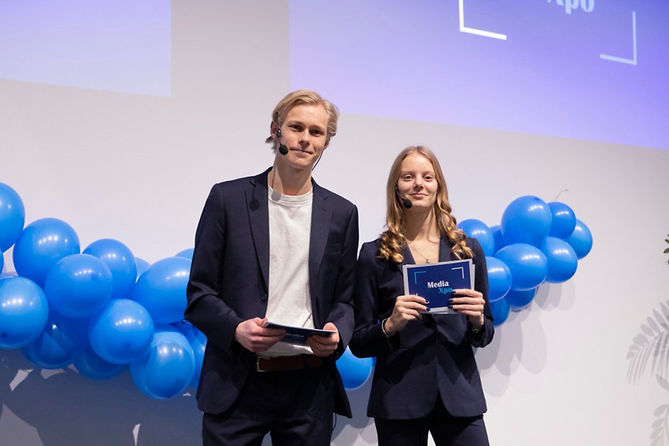 Studenter står på en scen framför publik och pratar. Foto.