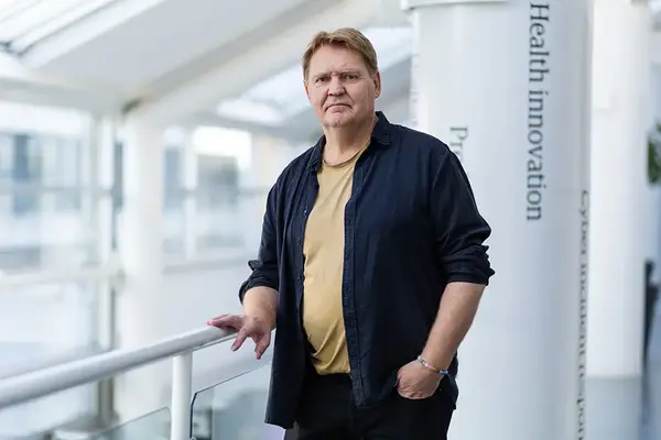 En person står vid ett räcke i inomhusmiljö och tittar in i kameran. Foto