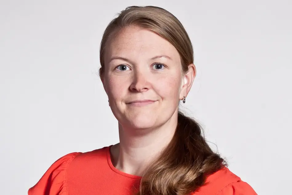 En kvinna i orange topp poserar för en bild. Foto