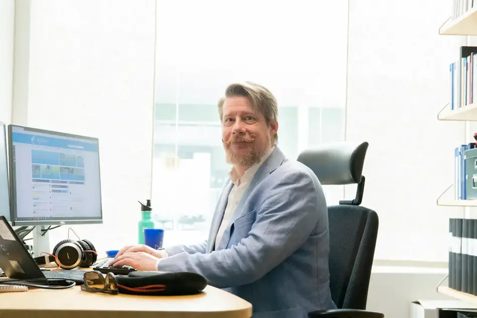 A man sitting at a desk, in front of a computer screen. Photo.