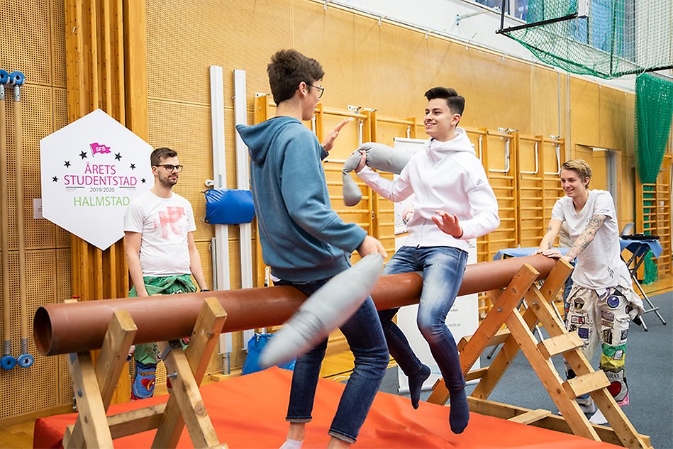 Två studenter sitter på en stock och står på varandra med laxar i tyg. Foto.