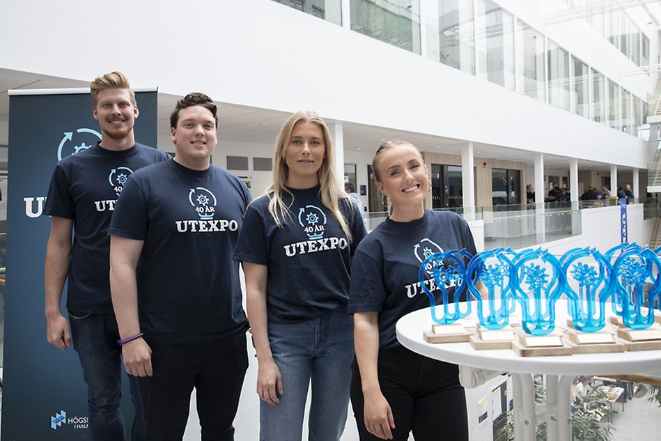 Four people standing next to each other in matching t-shirts in a bright building. Foto.