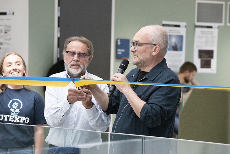 Two people are holding a pair of scissors cutting a yellow and blue ribbon. Photo.