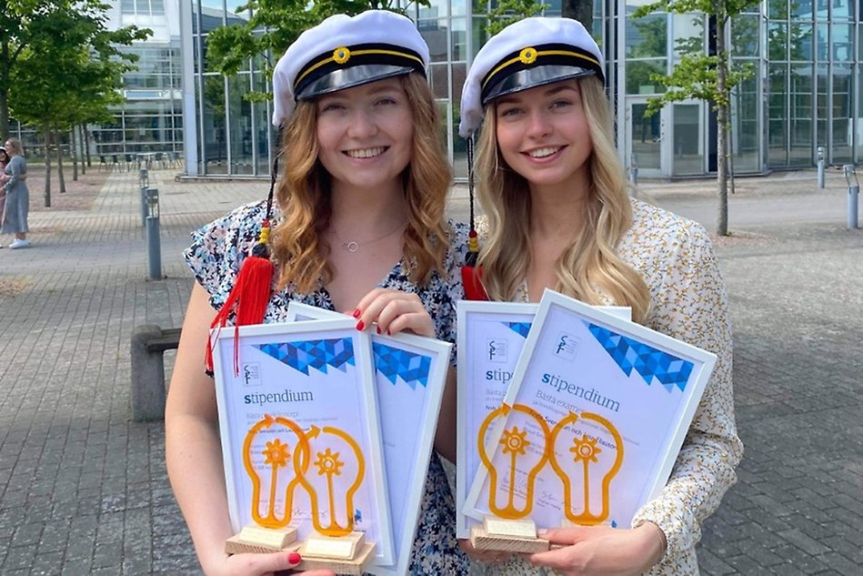 Två personer med studentmössor och diplom. Foto.