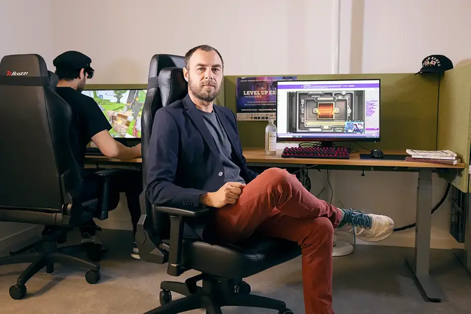 Man sittning in front of a computer sceen, looking into the camera. Photo