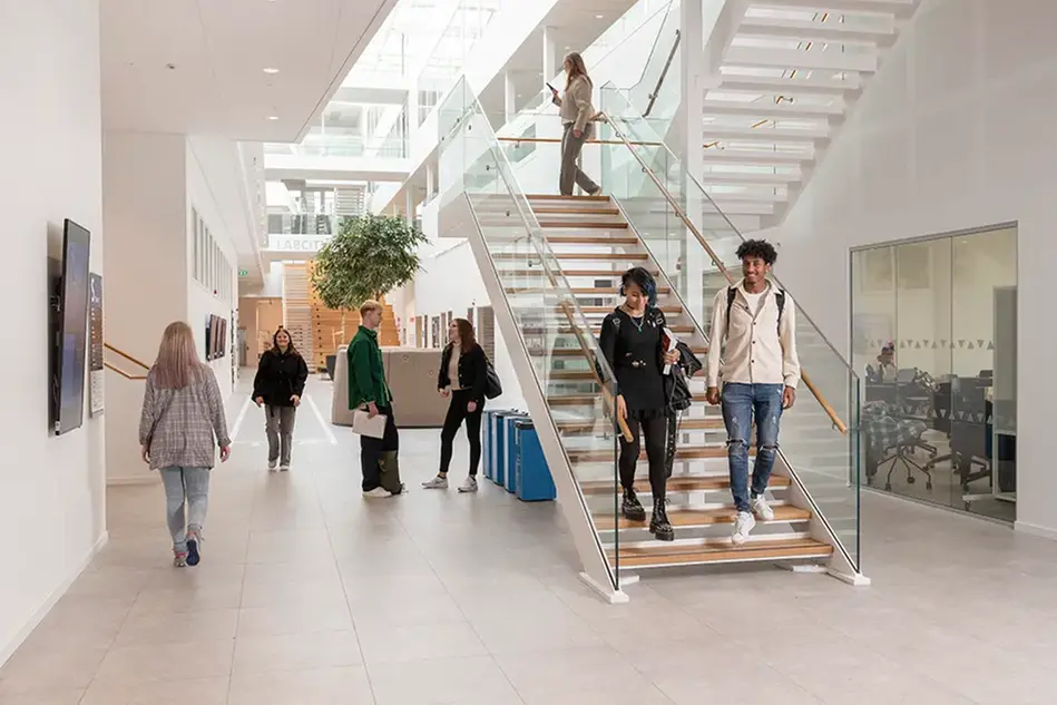 Students walking down the stairs in a building with brick walls and glass windows. Photo.