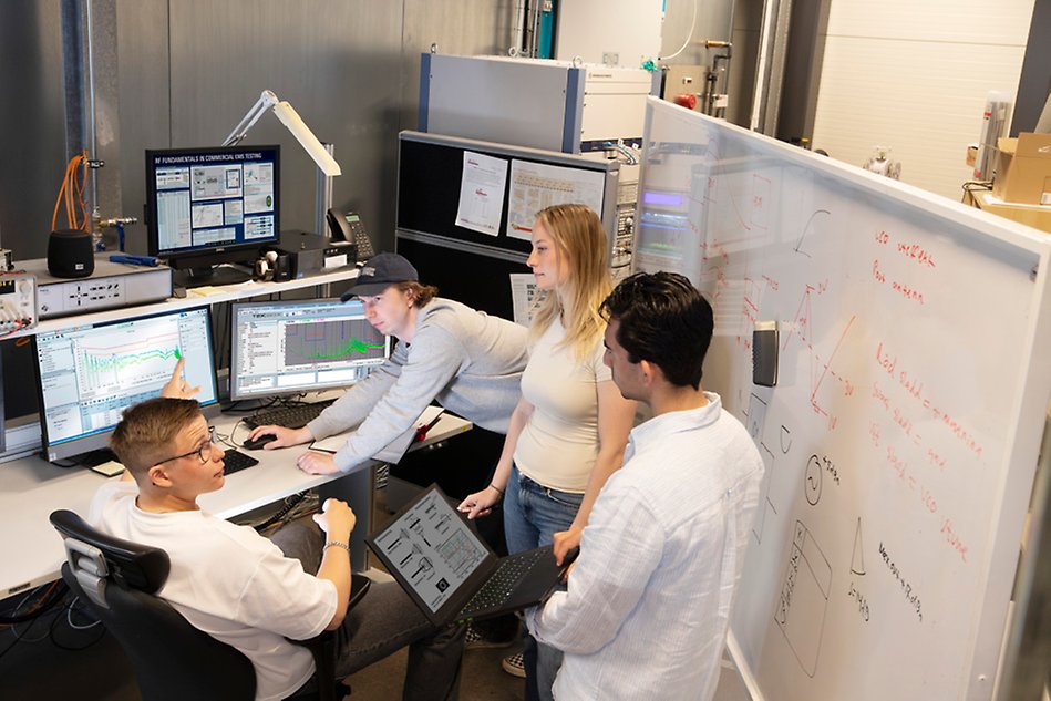 En grupp människor diskuterar vid en dator utanför en testkammare.