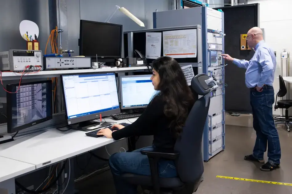 En person sitter vid ett skrivbord och en annan står i bakgrunden. 