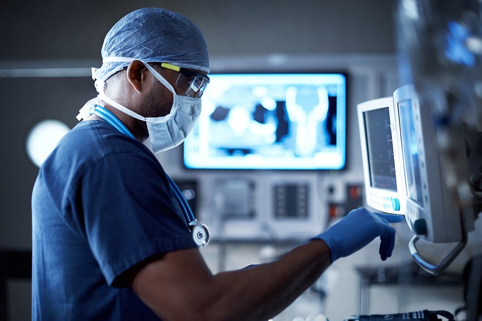 Person in facemask, in a hospital environment, reading on a screen. Photo.