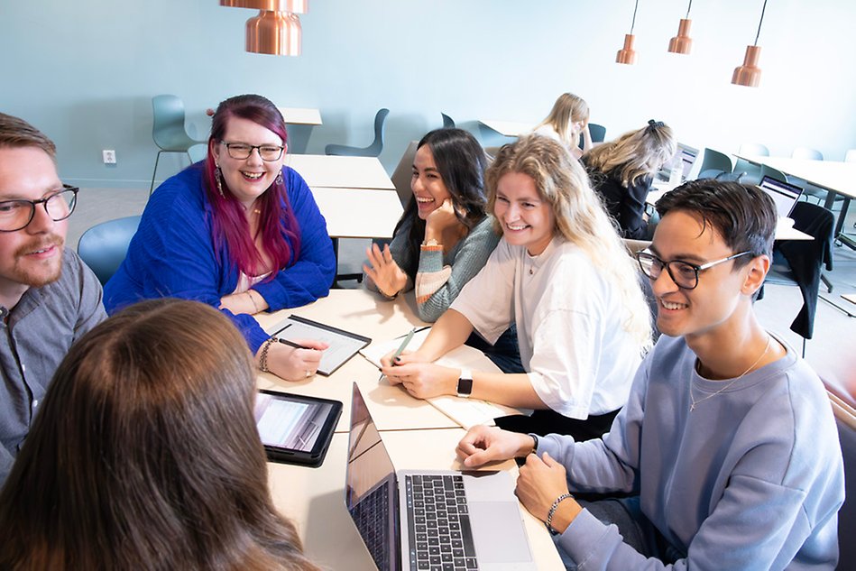 A group of students are sitting around a table, studying and laughing. Photo.