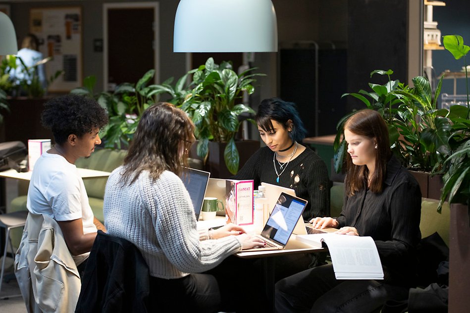Four students sitting around a table surrounded by green plants. Photo.