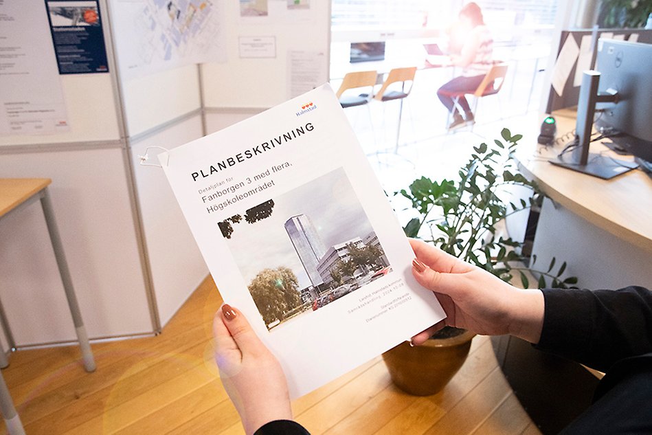 A compendium of the detailed plan is seen in the hands of someone looking at the exhibition. Photo.