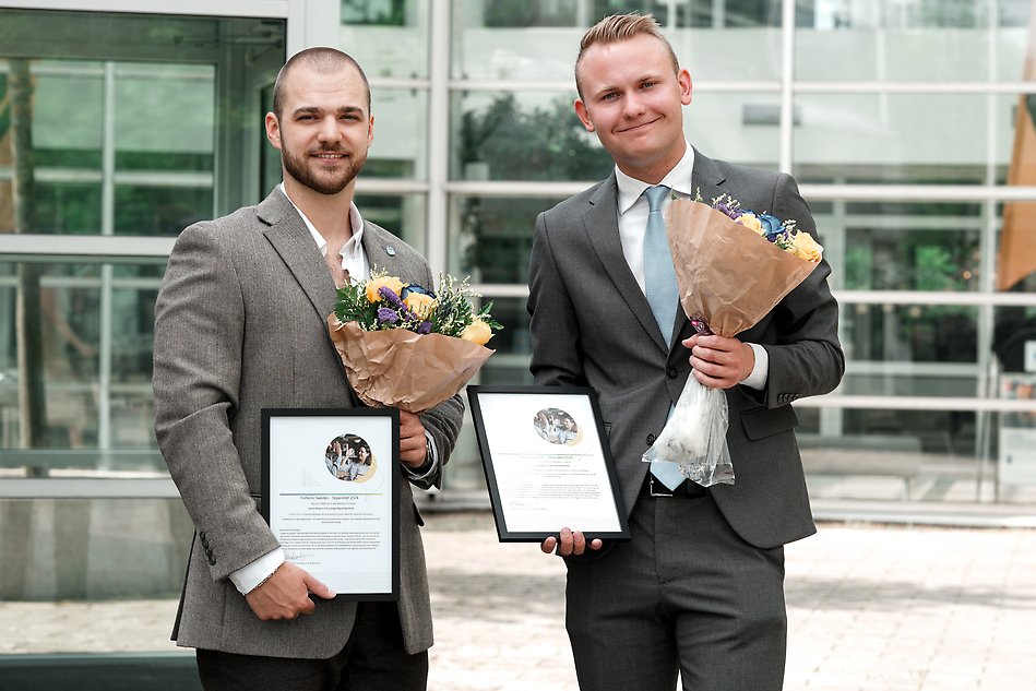 Två personer i kostym håller i diplom och blommor för att de fått Forterros stipendium. Foto.