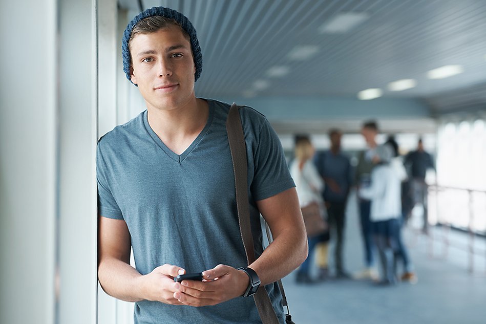 A young man with a phone in his hand is leaning against a wall. Photo.