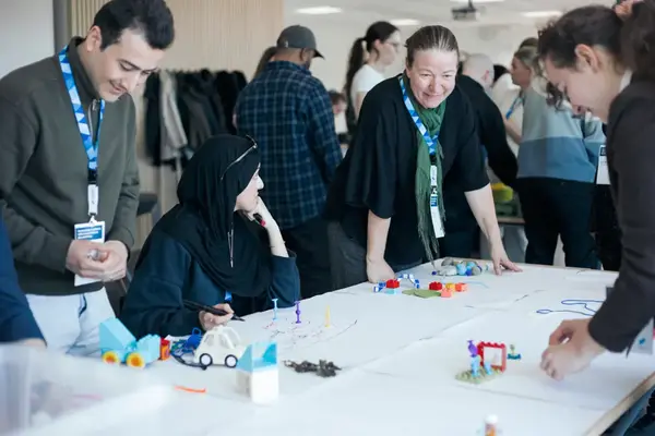 Grupp av människor står runt ett bord och bygger med lego.