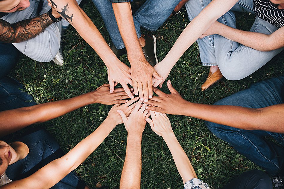 A group of people standing in a circle with their hands stretched out and touching in the middle.