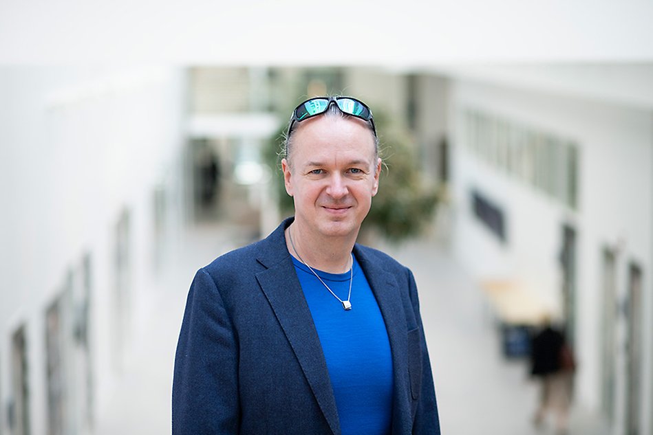 A person with blue shirt and a jacket is looking into the camera. Portrait photo.