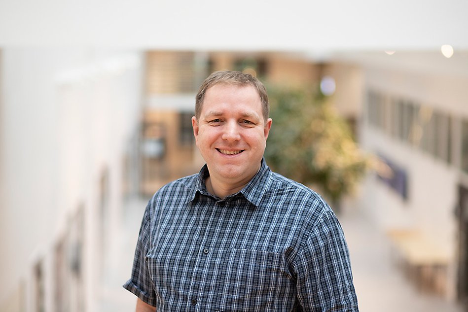 A man wearing a checkered shirt lookin gin to the camera. Photo.